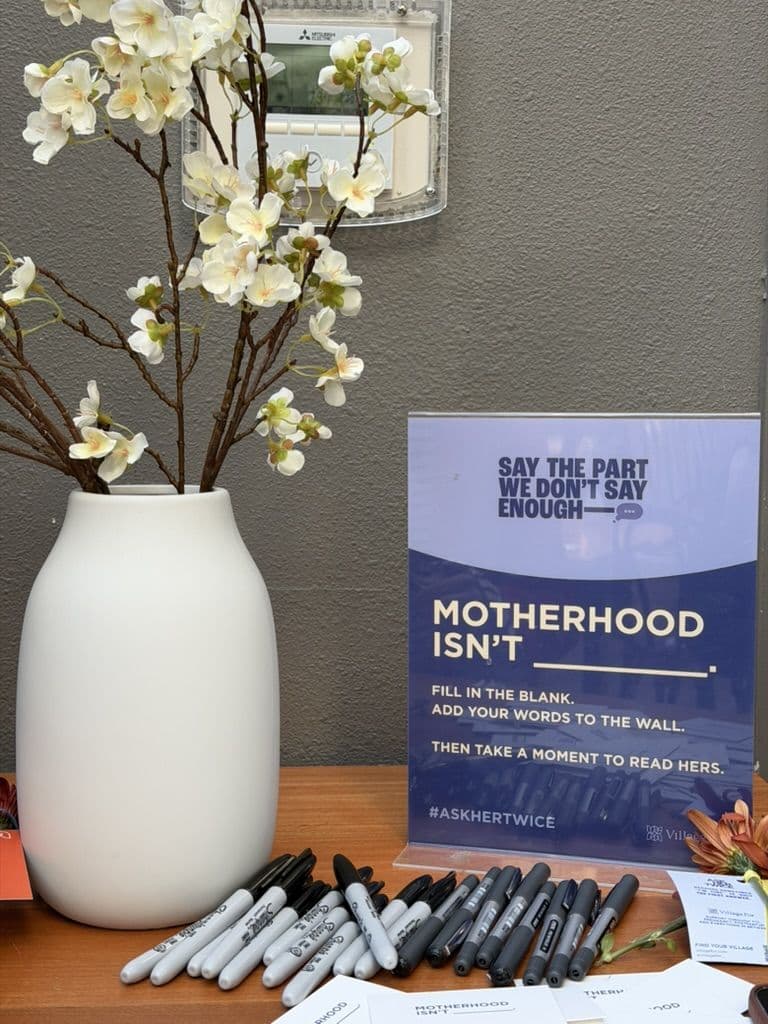 The Honor Wall station at the event: a card reading Motherhood isn’t, with markers ready for guests to fill in the blank