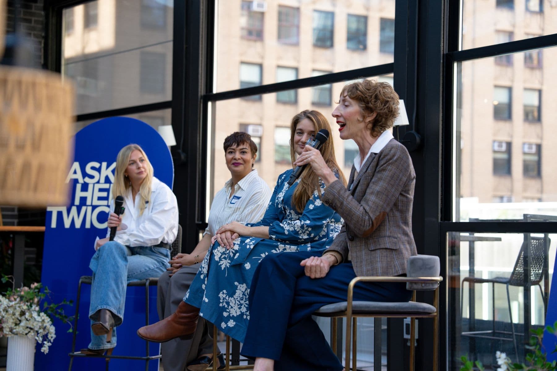 A panelist speaks into a microphone beside the Ask Her Twice banner while three other panelists listen
