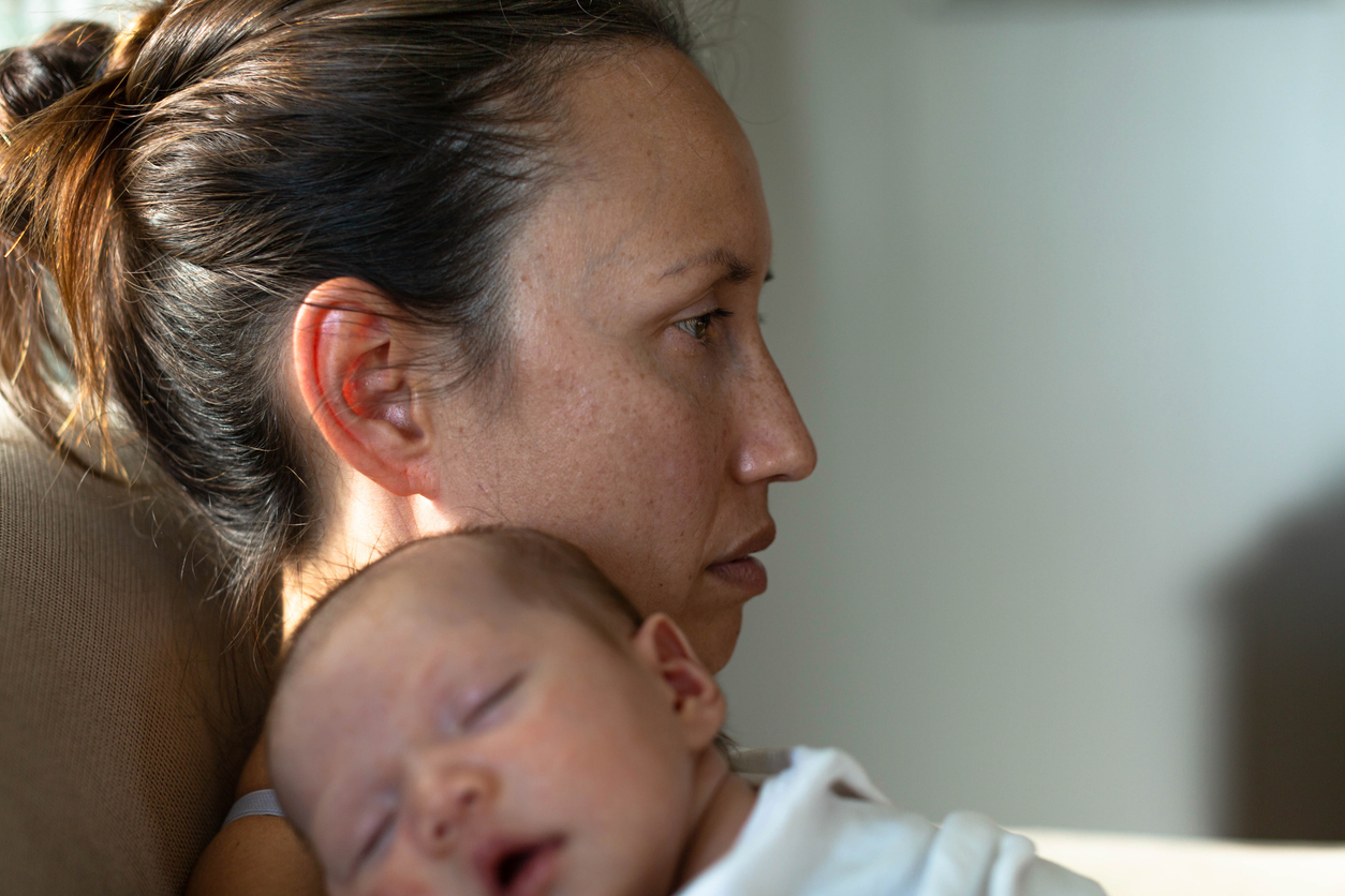 A new mother holding her sleeping baby, staring off with a distant expression