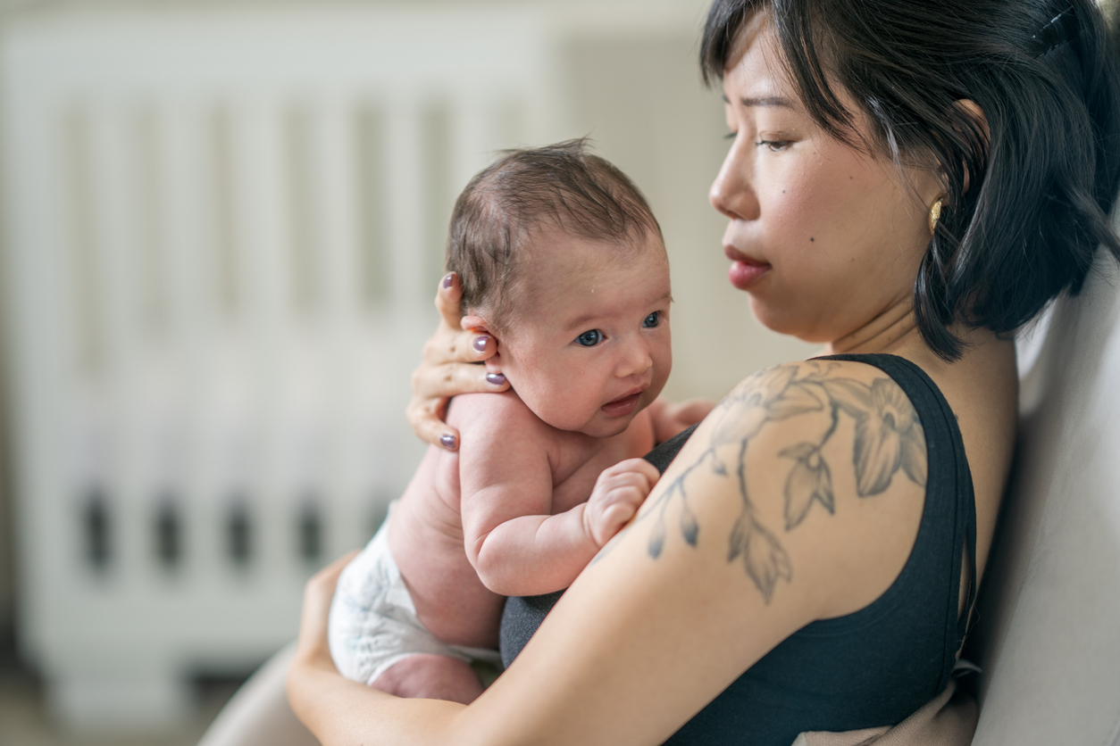 A mother holding her newborn close, a crib blurred softly in the background