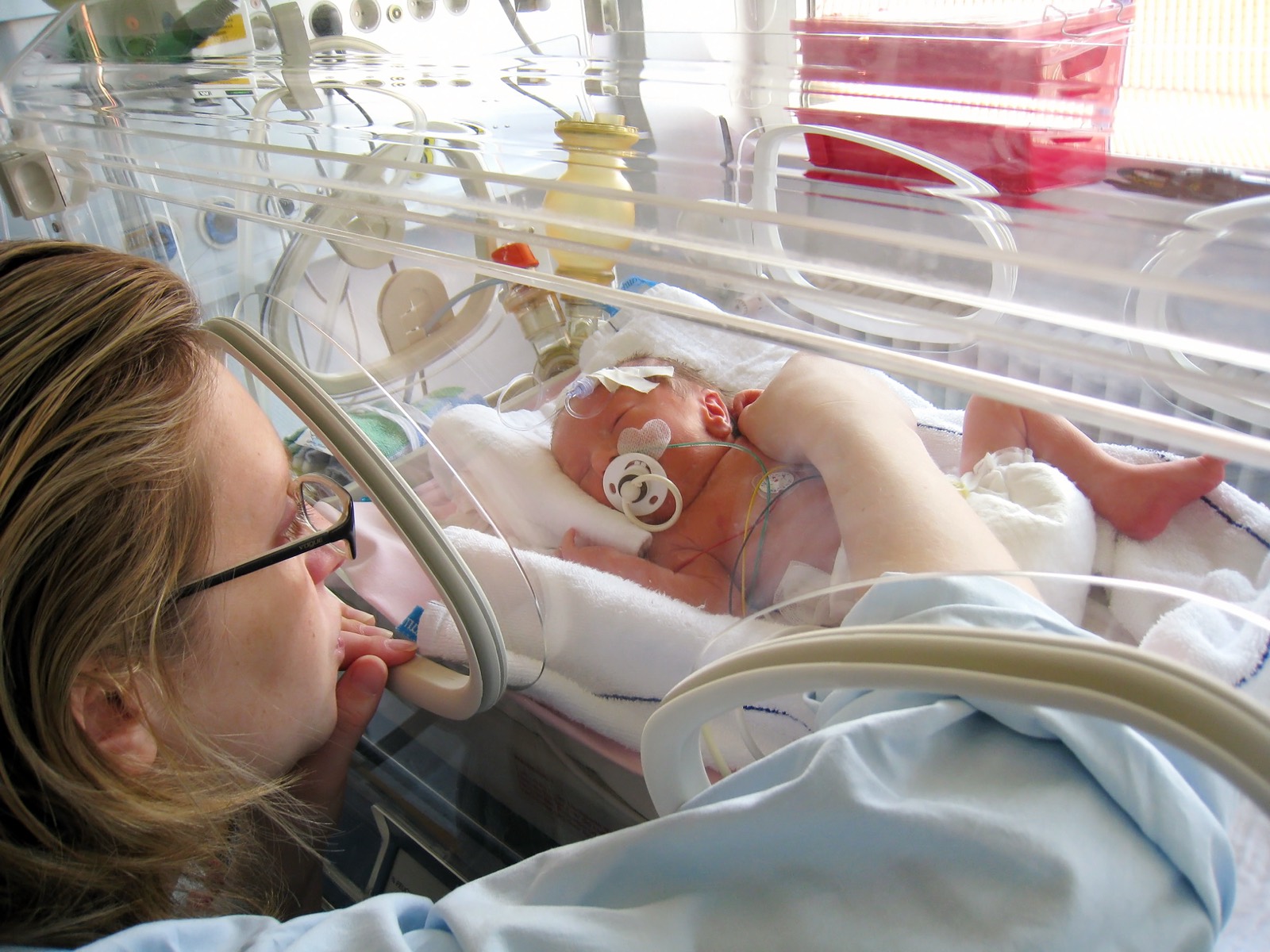 A mother leaning close to her baby in a NICU incubator